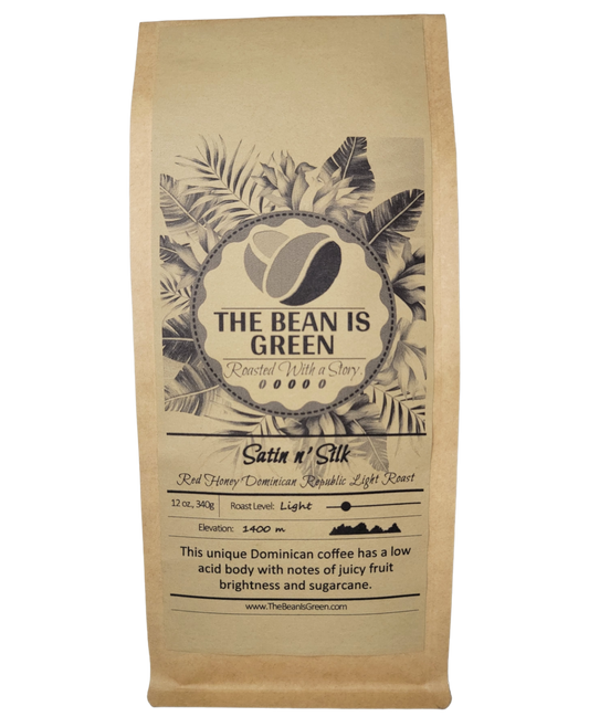 Brown kraft bag with The Bean Is Green grey-wash tropical logo. Satin n' Silk - Organic Red Honey Dominican Republic Light Roast Whole Bean Coffee. Elevation 1400m with graph shown. This unique Dominican coffee has a low acid body with notes of juicy fruit brightness and sugarcane. - website = www.thebeanisgreen.com